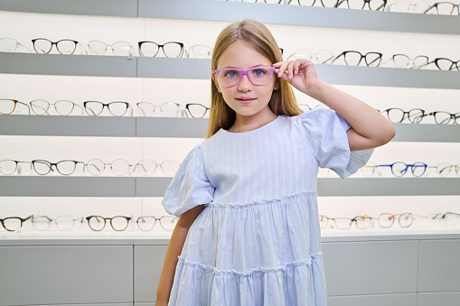 Confident young lady trying on new pair of glasses in optical store