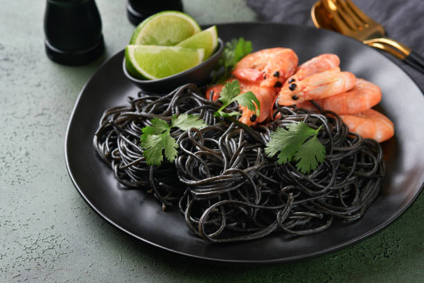 istock Black spaghetti pasta shrimp on black plate on dark concrete table background. Squid ink pasta with prawns. Pasta seafood. Top view on green stone table. Mediterranean traditional cuisine dish. 1669985837