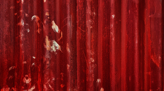 abstract old dark red galvanized corrugated metal sheet wall with rust used as background in close up view. grey rusty iron on red metal construction site wall.