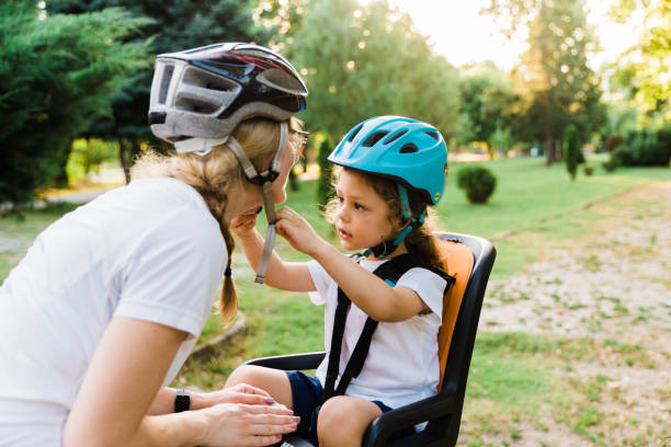 Mother helping son wearing helmet for cycling at park. Boy getting ready by wearing bike helmet to start cycling together with his mother
