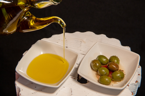 Drizzle of extra virgin olive oil from Spain, next to a plate of green olives. AOVE