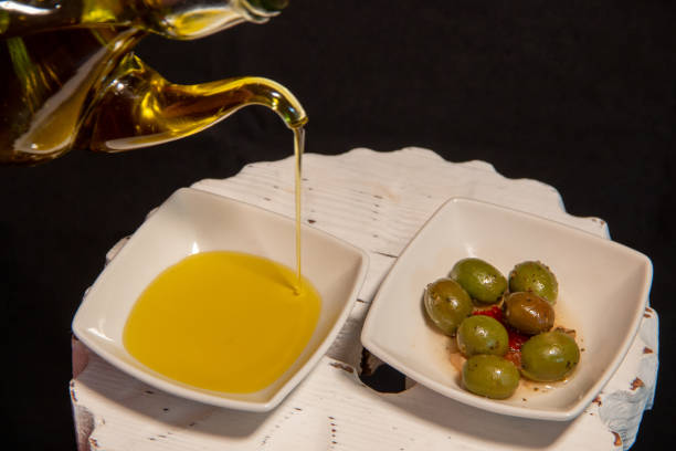 Drizzle of extra virgin olive oil from Spain, next to a plate of green olives Drizzle of extra virgin olive oil from Spain, next to a plate of green olives. AOVE olive oil pouring antioxidant liquid stock pictures, royalty-free photos & images