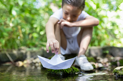 Child playing with paper boat in the water
