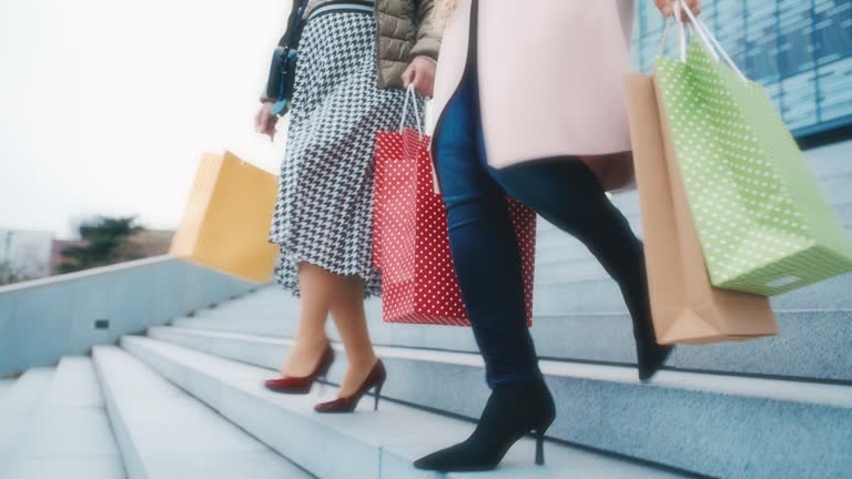 SLO MO Two unrecognizable women in stilettos carry shopping bags as they walk down the stairs in the city