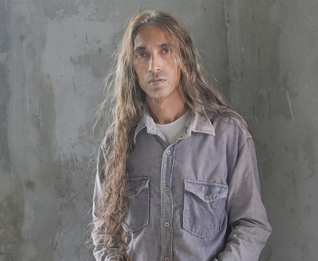 Man with tan skin and brown long hair posing in front of gray background