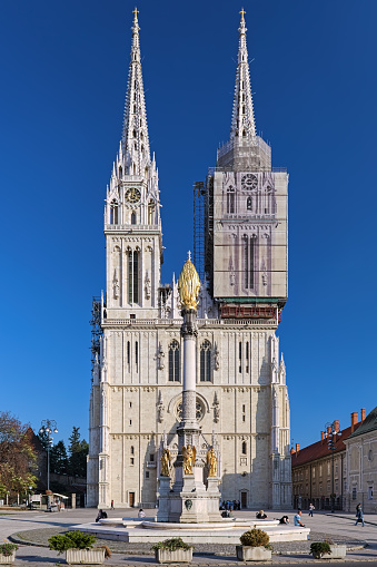 Zagreb, Croatia - October 10, 2018: Zagreb Cathedral and fountain of Blessed Virgin Mary in sunny clear day. The cathedral is dedicated to the Assumption of Virgin Mary and to kings Saint Stephen and Saint Ladislaus. It was laid in the 11th century. The present Neo-Gothic building is the result of restoration-reconstruction in 1880-1906 by architect Hermann Bolle. Statue of the Blessed Virgin Mary with four angels by sculptor Anton Dominik Fernkorn was erected in 1873 in the center of a fountain designed by Hermann Bolle.