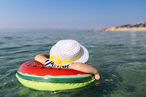 Rear view of fashionable young girl in inflatable watermelon float in ocean. Summer vacation travel concept.