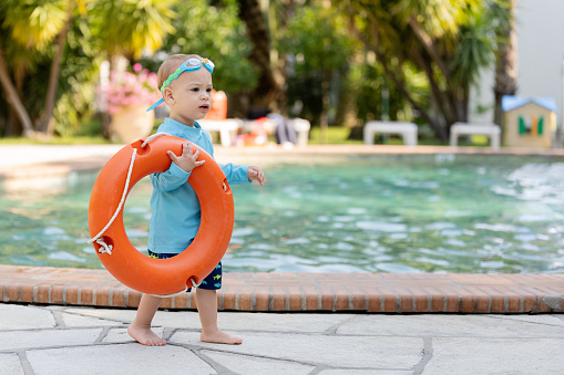 Young boy with goggles holding lifebuoy ring at the poolside. Space for copy.