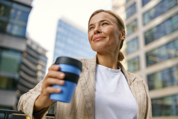 istock Female manager going to work while drinking coffee on office building background and looks away 1670258360