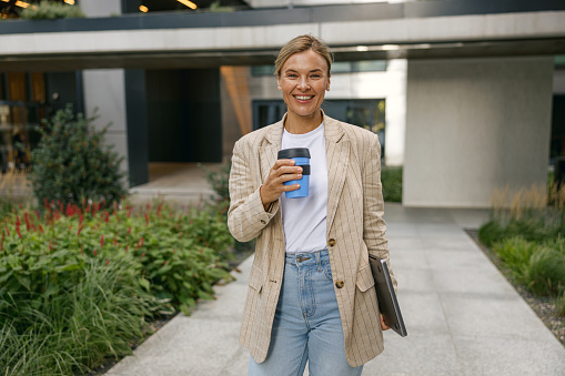 Female manager going to work while drinking coffee on office building background. High quality photo