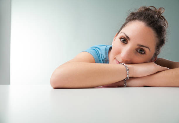 young woman in a blue shirt leans gently on her arms atop an office table, serving as her cushion. She's serenely reflective, contemplating her life's importance and what gives her existence meaning b
