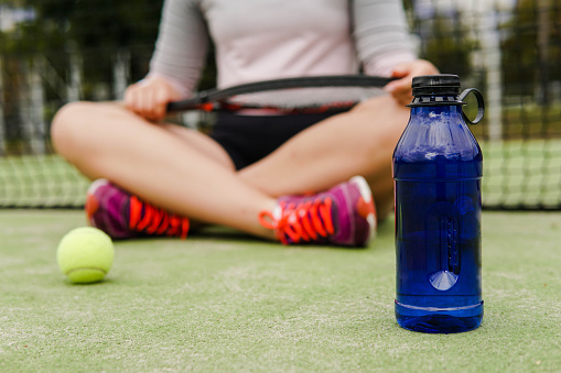 istock Bottle of water in front young woman tennis player sitting on the court. 1670273639