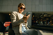 Pretty female entrepreneur in eyeglasses use phone while sitting in modern coworking space