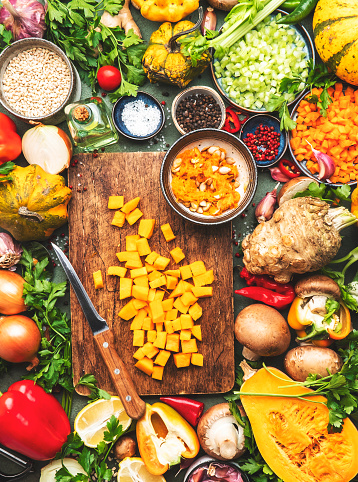 Food background. Diced raw peeled pumpkin and vegetable knife on rustic wooden cutting board. Vegetables, mushrooms, roots, spices - ingredients for vegan cooking. Healthy eating, diet, comfort slow food concept. Top view