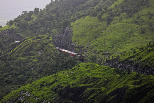 Indian Railway train traveling through the mountains in Western ghat.  Monsoon season and landscape is green