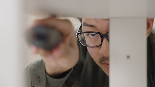 Close up shot of Asian man using a screwdriver to assemble the furniture