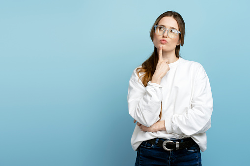 Pensive woman wearing eyeglasses having idea, looking for solution isolated on blue background. Portrait of smart student looking away, copy space. Education concept