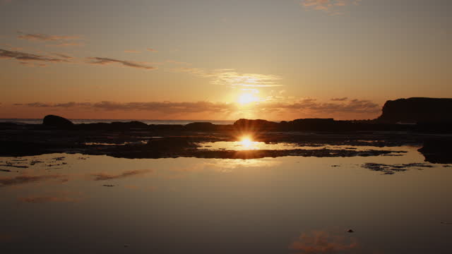 Timelapse of sun rising over the ocean reflected on still water on the coast