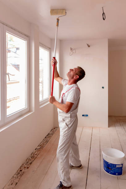 istock A man painting a white wall and celling, with paint roller in empty room 1670501150