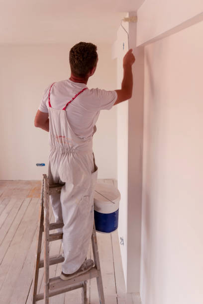 istock A man painting a white wall and celling, with paint roller in empty room 1670501154