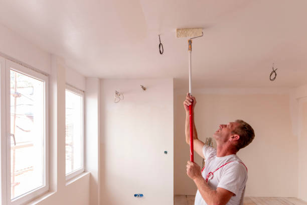 istock A man painting a white wall and celling, with paint roller in empty room 1670501159