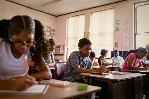 Black students attend an English class at school.  They sit down at desks to practice penmanship and discuss a book they have read.