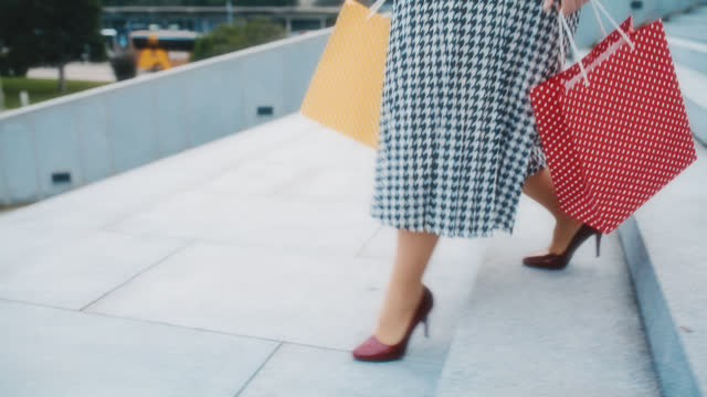 SLO MO An unrecognizable woman in skirt and stilettos carries shopping bags as she walks down the stairs in front of a modern building
