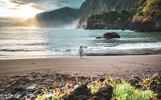 Description: Woman walking on beautiful beach and enjoying the atmospheric morning atmosphere. Seixal beach, Madeira Island, Portugal, Europe.