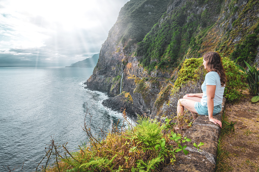 Description: Sporty woman looking at waterfall flowing into the sea in atmospheric morning atmosphere. Viewpoint Véu da Noiva, Madeira Island, Portugal, Europe.