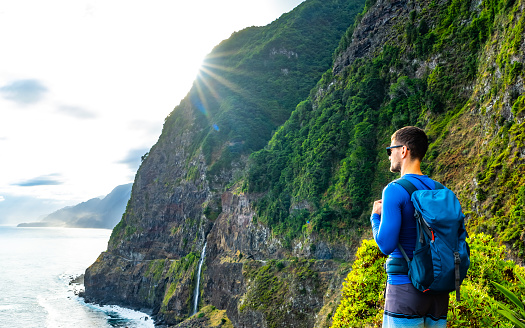 Description: Sporty man looking at waterfall flowing into the sea in atmospheric morning atmosphere. Viewpoint Véu da Noiva, Madeira Island, Portugal, Europe.