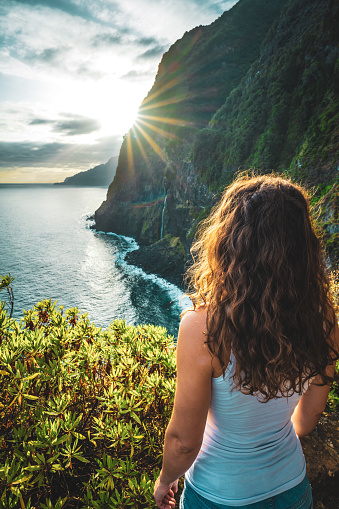 Description: Sporty woman looking at waterfall flowing into the sea in atmospheric morning atmosphere. Viewpoint Véu da Noiva, Madeira Island, Portugal, Europe.