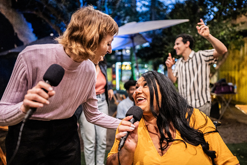 Friends singing together on karaoke at pub - wheelchair mature woman