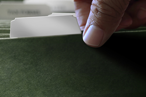 A male hand removes a file folder from a file cabinet. The category tab is blank.