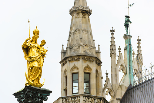 Virgin Mary statue on Marienplatz square by Town Hall, Munich, Germany. This place is top landmark of Munich. Golden sculpture atop Mariensaule column on background of in Munich city center.