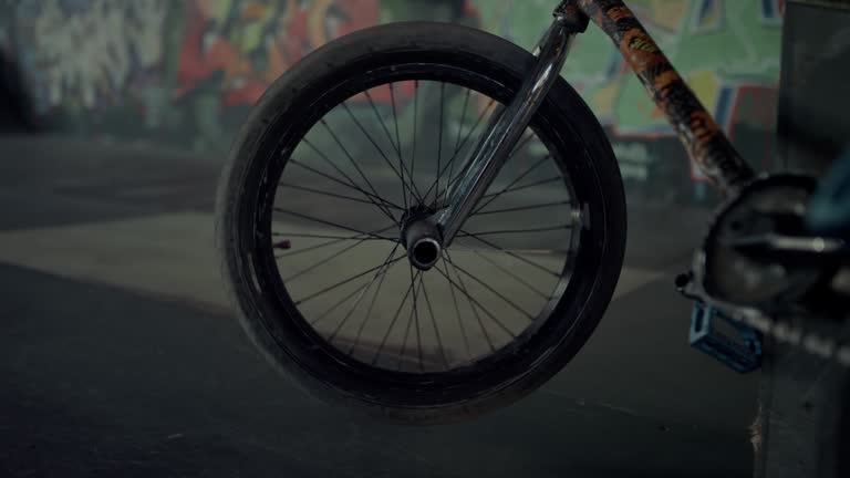 Bmx bicycle wheel spinning at skatepark with graffiti wall. Bike parking.