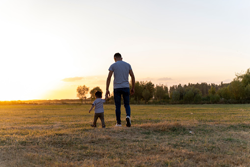 Playful young father and little son enjoying sunny afternoon in nature. Father and son on meadow. Copy space.