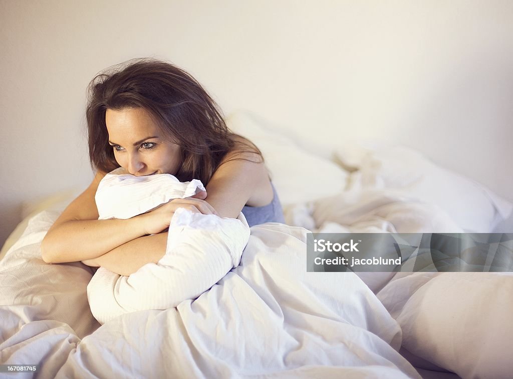 Sitting Alone on Bed Thinking of You Pensive woman smiling and sitting alone on bed thinking of someone Adult Stock Photo