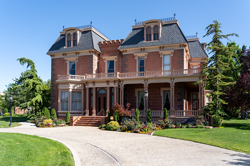 Luxury Home in Chatham, Cape Cod, Massachusetts, USA.  Beautifully landscaped front yard with flowers, lush grass and bushes is in foreground. Chairs are on the porch. Trees frame the house on both sides.