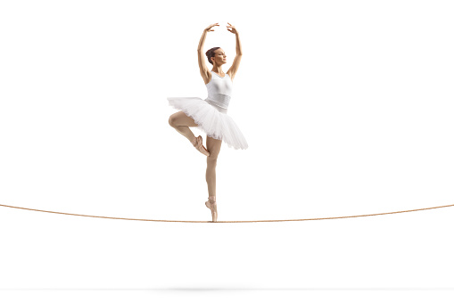Full length shot of a ballerina dancing on a tightrope isolated on white background