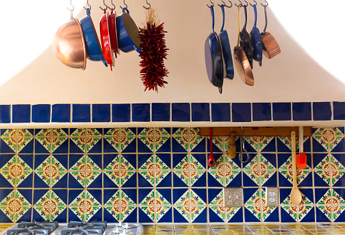 Kitchen brass utensils, chef accessories. Hanging copper kitchen with white tiles wall flower vase window and olive oil
