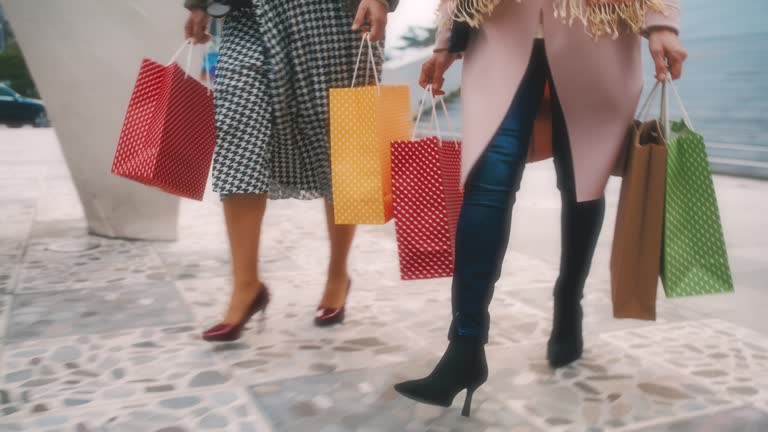 SLO MO Two unrecognizable women in stilettos carry shopping bags as they walk down the stairs in front of the mall in the city