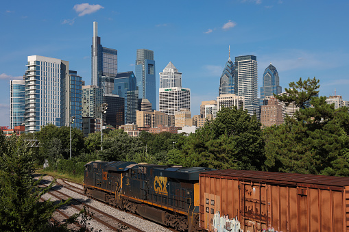 Philadelphia, Pennsylvania, USA - Sep 2, 2023: A CSX train on railroad tracks with Philadelphia skyline in the background
