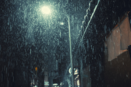 In the midst of heavy rain, the streetlights illuminated the raindrops, and there was a faint glow coming from the entrance of a Japanese restaurant nearby.