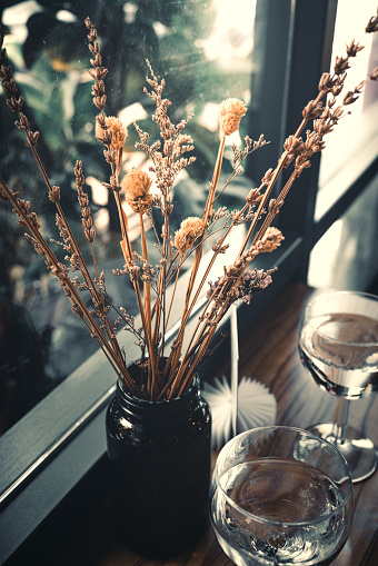 A softly lit small table by the window, adorned with decorations of dried plants and a glass water cup.