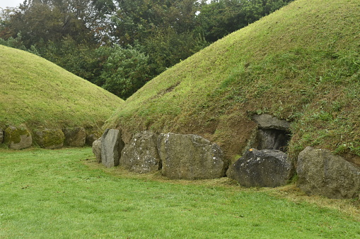 A pair of grass covered passage tombs in the form of mounds, surrounded by kerbstones, on a wet day at Knowth, part of the Brú na Bóinne complex.