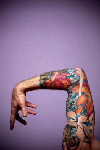 mid adult man's bent arm at elbow with tattoo sleeve of flowers and hand posed.  vertical composition.