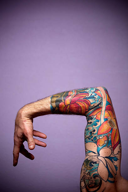 tattoo mid adult man's bent arm at elbow with tattoo sleeve of flowers and hand posed.  vertical composition. forearm tattoos men stock pictures, royalty-free photos & images