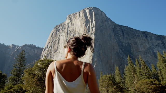 Young attractive woman walking trail in meadow looking up at rock face in Yosemite National Park