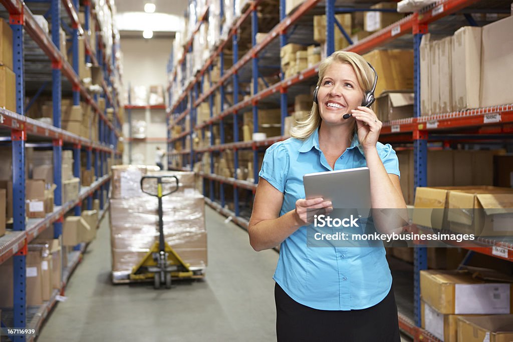 Woman holding a tablet with headphones on in a warehouse Businesswoman Using Digital Tablet In Distribution Warehouse Using Headset Headphones Stock Photo