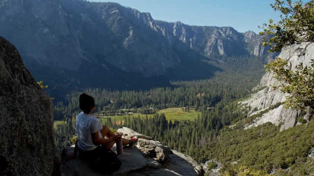 Young attractive woman sitting on cliff edge overlooking vast valley and mountain View